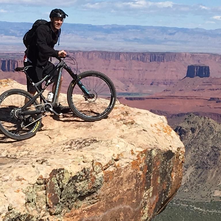 Andy Singleton mountain biking on a cliff edge above a desert canyon